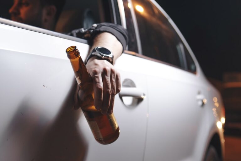 Driver holding a beer bottle in car highlighting risk of drunk driving accidents in Murfreesboro.