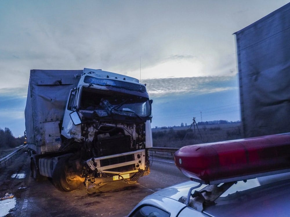 Image shows a heavily damaged truck at an accident scene with a police vehicle nearby, illustrating how photos of vehicle damage help reconstruct what happened and determine fault.