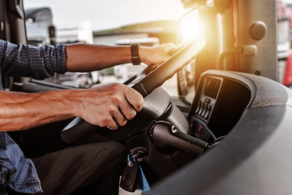 Image shows a truck driver holding the steering wheel inside the cabin, highlighting how driver behavior and control can help prove fault in a truck accident.