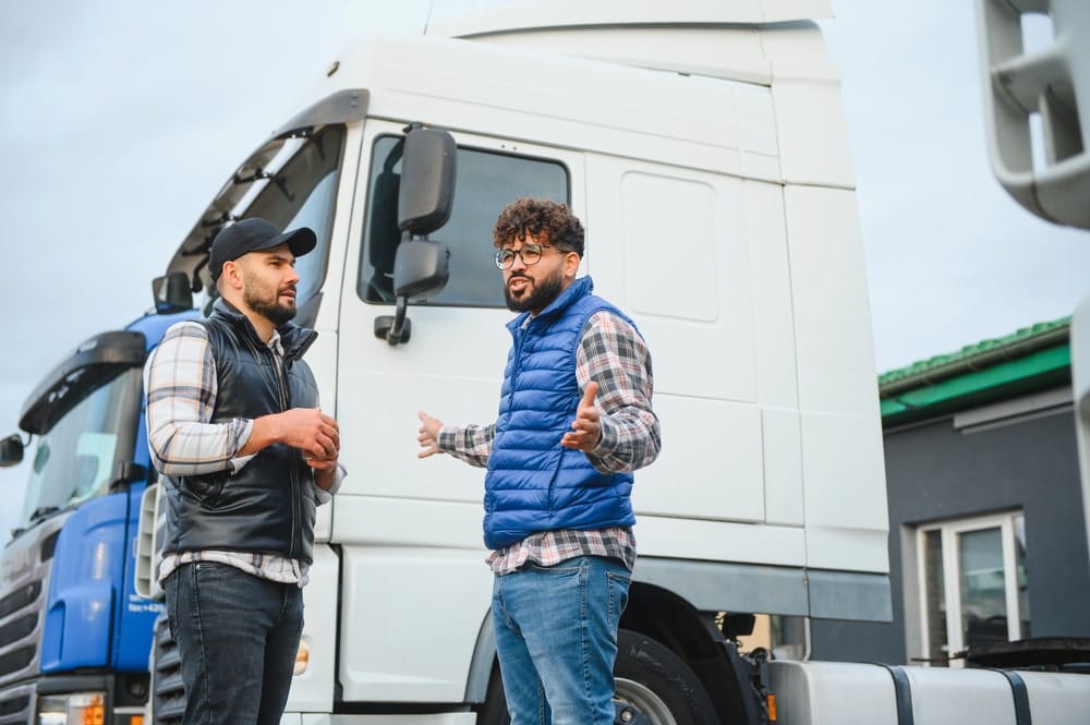 Image shows two truck drivers talking beside a commercial truck, suggesting witness statements and firsthand accounts that help investigators prove fault in a truck accident.