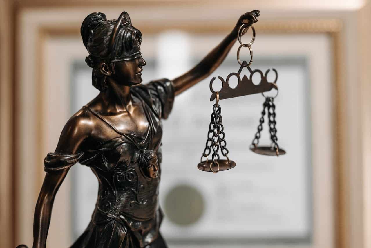 Image is of a bronze Lady Justice statue holding balanced scales, symbolizing legal standards involved in motorcycle injury claims.
