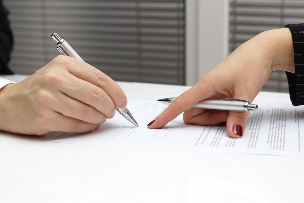 Image is of two individuals reviewing and signing legal documents, concept of motorcycle accident settlements and agreement negotiations
