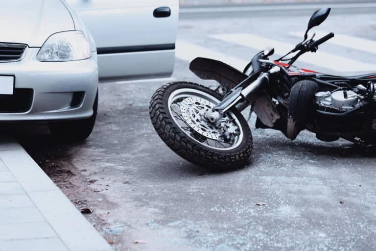 Image is of a motorcycle lying on the roadway next to a damaged car after a collision, concept of car accidents in Murfreesboro involving motorcycles.