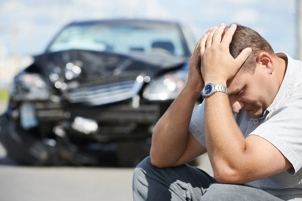 Image is of an accident victim sitting in distress near a damaged vehicle, concept of uninsured drivers in Tennessee and post crash uncertainty.