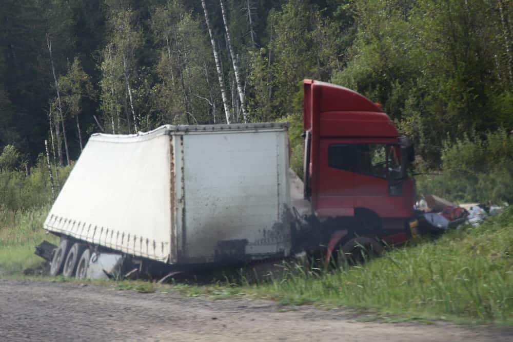 Image is of a damaged semi truck off the road in a wooded area, showing a Jackknife Truck accident in Murfreesboro