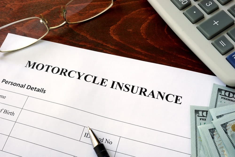 Image is of a motorcycle insurance document next to a stack of hundred dollar bills, concept of a motorcycle accident settlement.