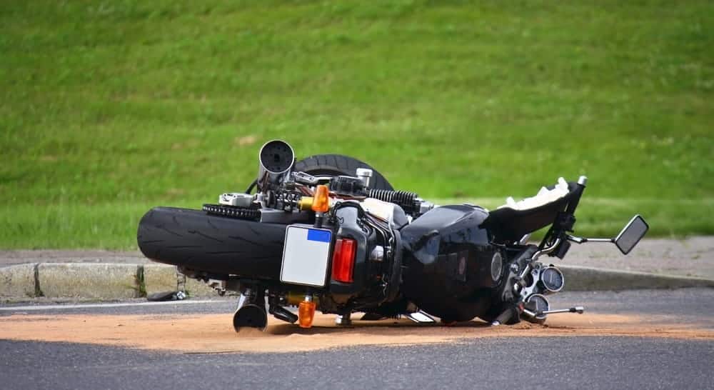Image is of a black motorcycle lying on its side on a road with debris, concept of the immediate aftermath of a motorcycle accident.