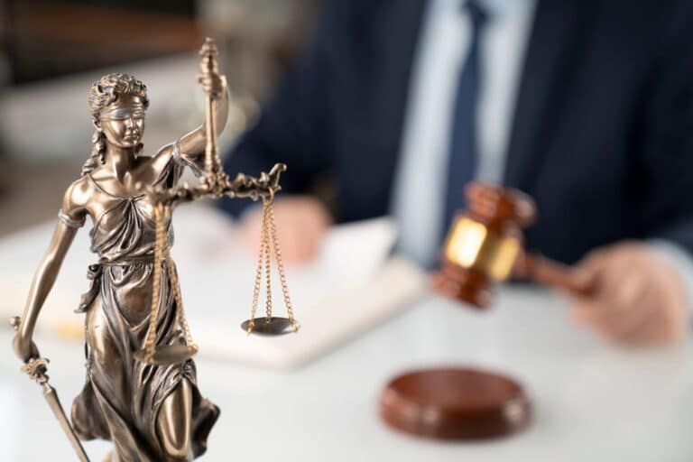 Image is of a Lady Justice statue with a lawyer or judge in the background using a gavel, concept of legal representation for a motorcycle accident.