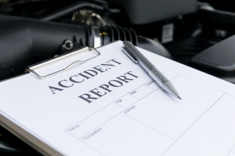 Image is of an accident report form on a clipboard near a vehicle engine, highlighting documentation used in a motorcycle accident claim