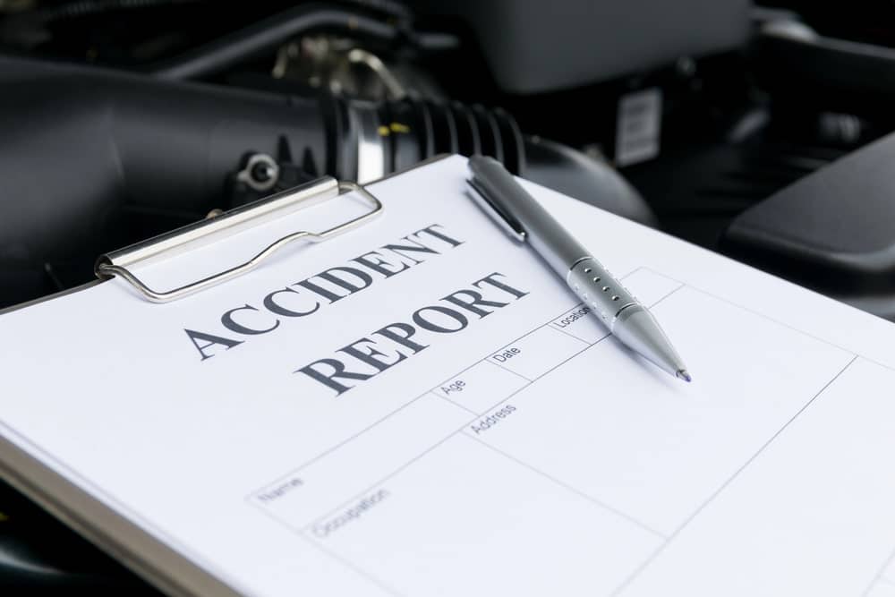 Image is of an accident report form on a clipboard near a vehicle engine, highlighting documentation used in a motorcycle accident claim