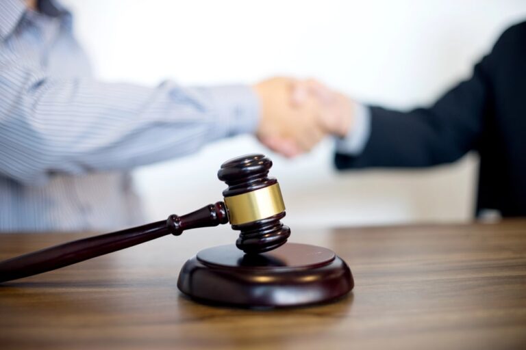 Image is of a legal handshake with a gavel on the table, concept of car sccident settlements and final case resolution