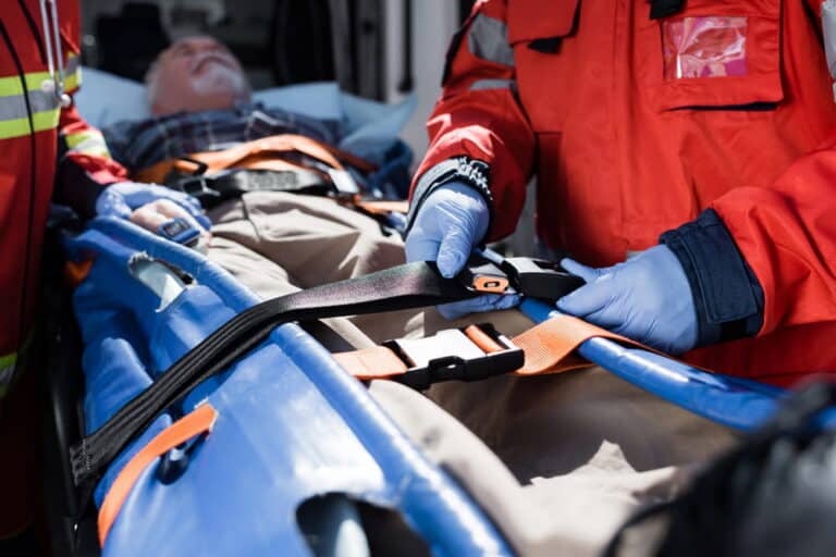 Image is of emergency responders securing a patient on a stretcher, representing urgent care after a car accident