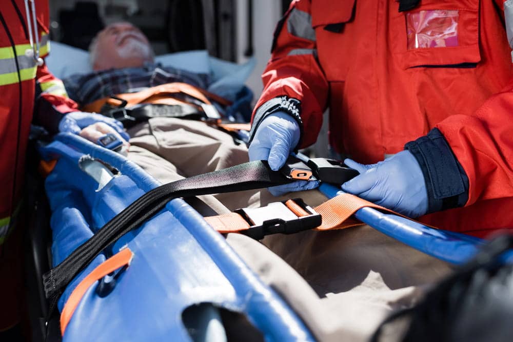 Image is of emergency responders securing a patient on a stretcher, representing urgent care after a car accident