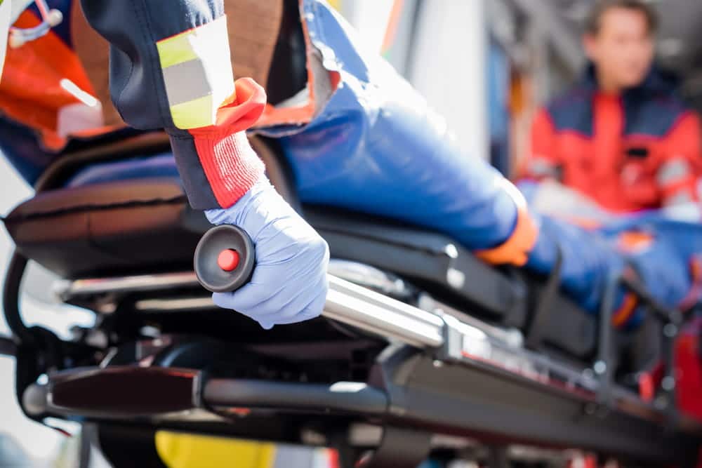 Image is of paramedics moving a patient on a stretcher, highlighting immediate medical support following a car accident