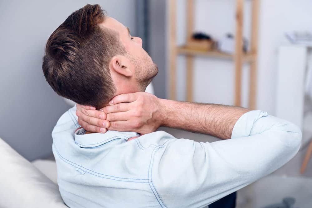 Image is of a person holding their neck in pain, concept of delayed injuries after a car crash affecting the neck and soft tissue