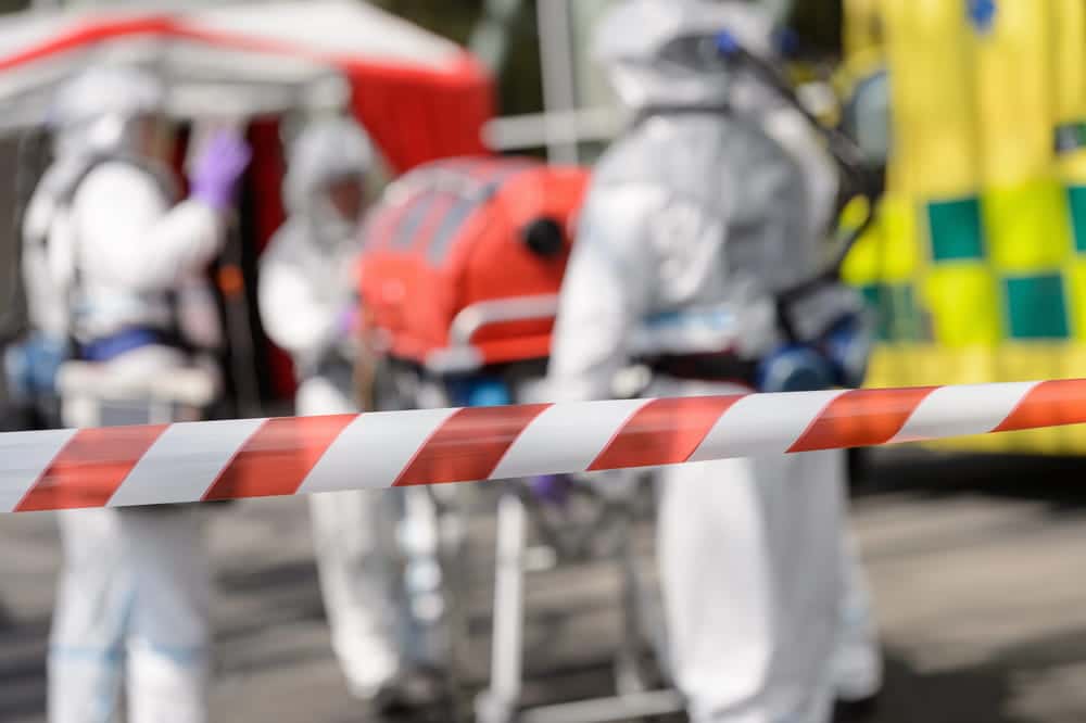 Image is of emergency hazmat crews responding behind safety tape after a truck crash involving hazardous material exposure.