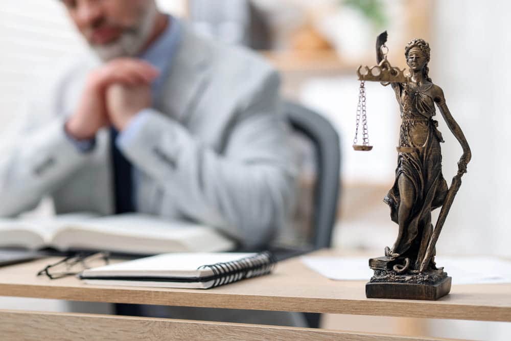 Image is of a legal professional reviewing case documents beside scales of justice, concept of car accident litigation.