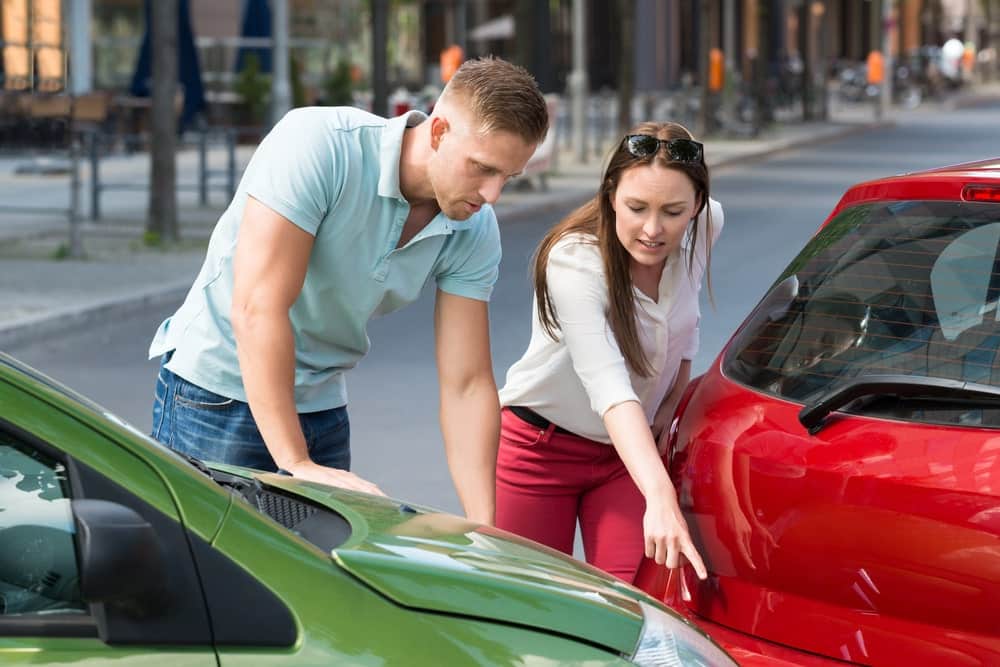 Image is of drivers examining vehicle damage after a roadway collision, concept of car accident litigation.