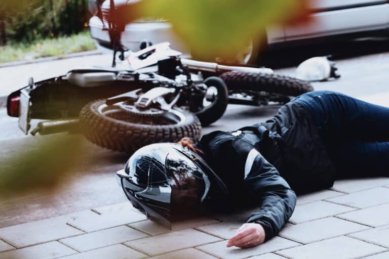 Image is of a motorcyclist lying on the ground after a roadway collision, representing serious injuries associated with fatal motorcycle accidents.