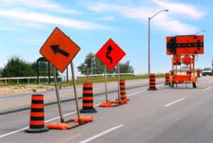 Image is of road construction signs, traffic barrels, and lane changes, concept of a motorcycle accident involving construction zone hazards and roadway obstacles.