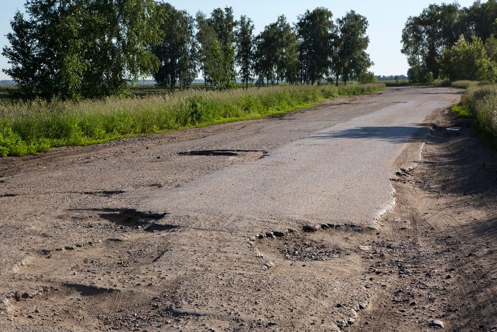 Image is of a roadway with multiple potholes and deteriorated pavement, concept of a motorcycle accident caused by dangerous road conditions in Tennessee.