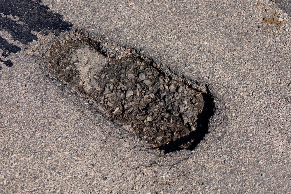 Image is of a large pothole in the roadway, concept of a motorcycle accident resulting from pavement defects and unsafe road surfaces.