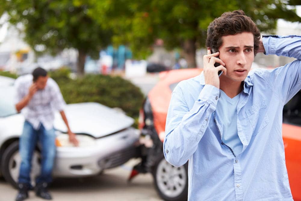 Image is of a driver making a phone call after a collision, concept of a car accident involving teen drivers and crash response.