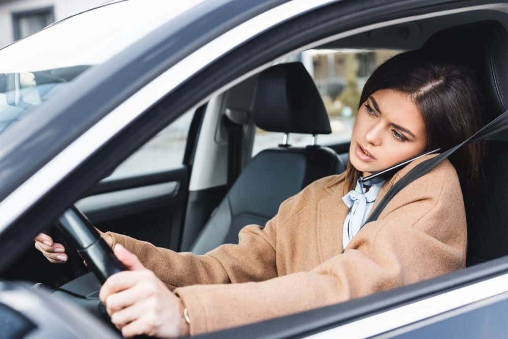 Image is of a driver using a mobile phone behind the wheel, concept of distracted driving in Tennessee.