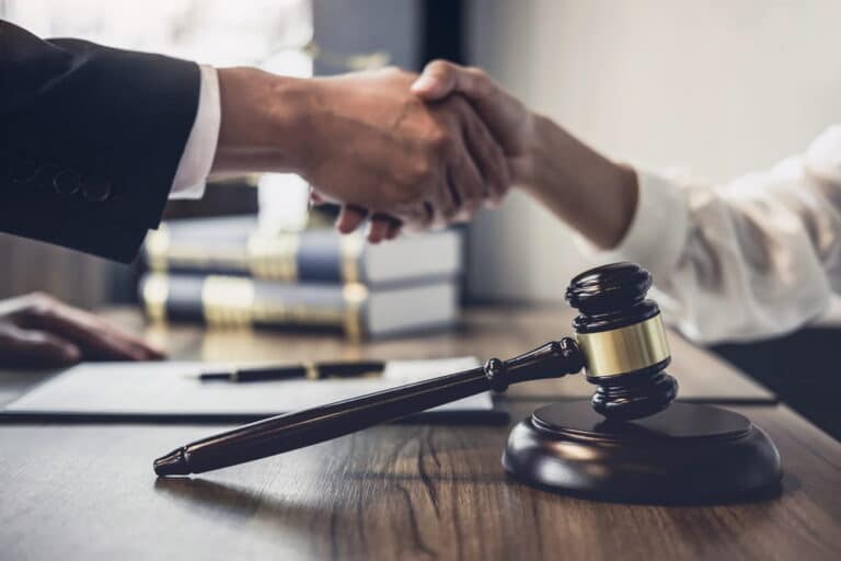 Image is of two people shaking hands beside a judge's gavel, concept of settling a truck accident lawsuit in TN.
