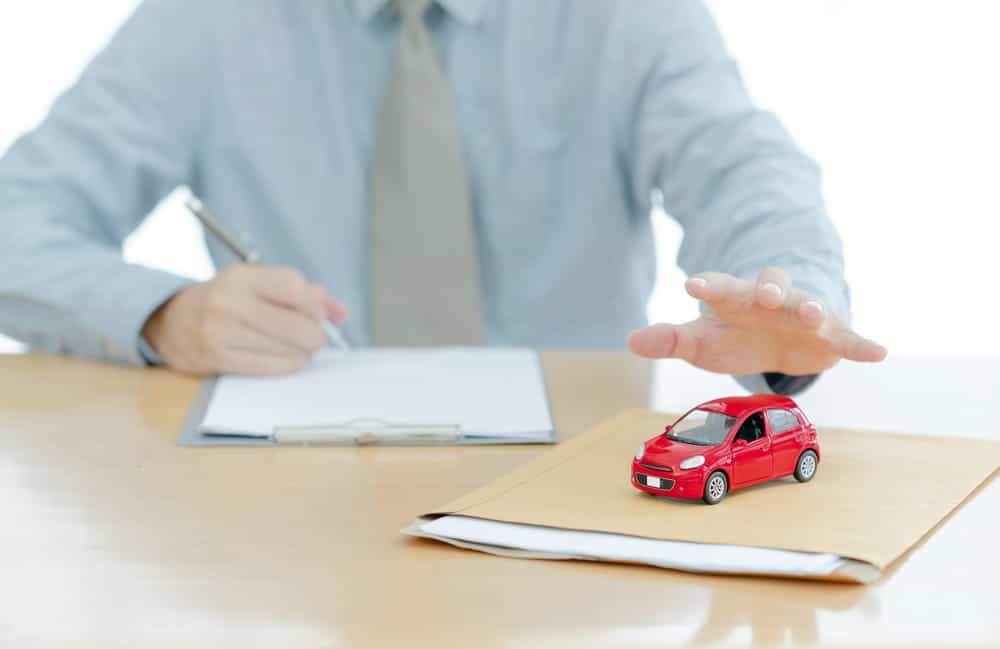 Image is of an insurance representative reviewing claim documents with a model car, concept of a chain reaction accident claim in Murfreesboro.