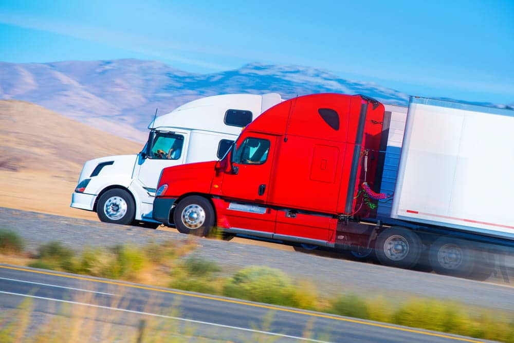 Image is of two semi trucks traveling side by side, concept of truck blind spot collision risks