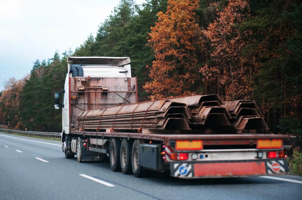 Image is of a flatbed truck transporting secured metal materials, concept of cargo spill hazards on Tennessee roads.