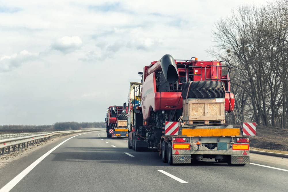 Image is of a commercial truck transporting heavy machinery on a highway, concept of cargo spill risks on Tennessee roads.