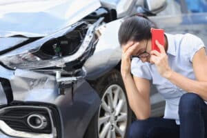 Image is of a driver making a phone call beside a damaged vehicle, concept of reporting a car accident in TN.