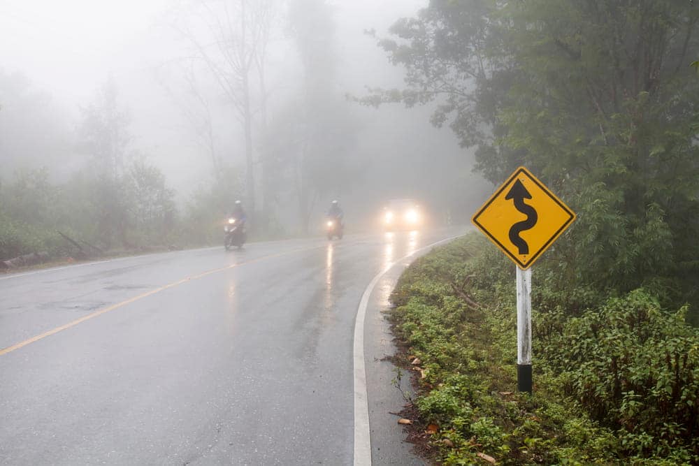 Image is of motorcycles traveling on a wet road in heavy fog, concept of poor visibility causing motorcycle accidents in TN.