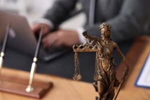 Image is of a lawyer working on a laptop behind a Lady Justice statue, concept of legal research and case preparation following a truck accident in TN.